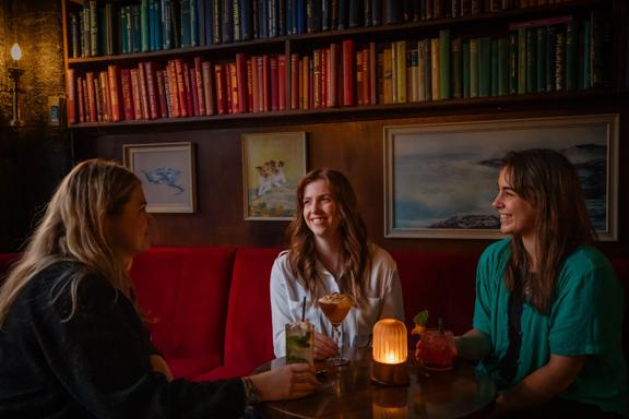 Three people sit at a table enjoying drinks at The Library, a cocktail bar in Te Aro, Wellington.