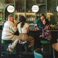 Interior of Hummingbird restaurant in Wellington, with guests seated at a green-tiled bar while a staff member prepares drinks behind the counter, shelves of bottles and glassware illuminated by warm, ambient lighting.