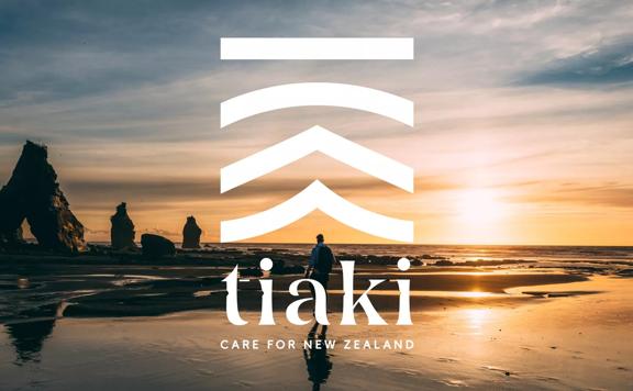 The Tiaki Promise logo in white laid over a scenic beach at sunset.