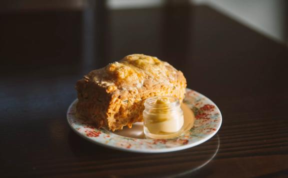 A cheese scone and a tiny jar of butter or a small plate with a blue rimmed plate with a pink floral pattern on a dark wood table at Floriditas, a restaurant on Cuba Street in Te Aro, Wellington. 