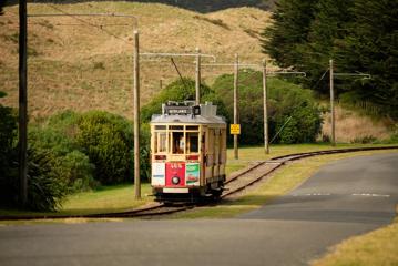 An old schol red and yellow tram beside a path in Queen Elizabeth Park, Kāpiti Coast.