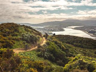 A scenic view of Porirua Harbour from  Colonial Knob Walkway on Mount Rangituhi. A cyclist is riding their mountain bike on the trail.