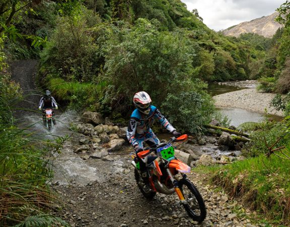 Two riders on motorbikes passing through a stream on the Karapoti Challenge course