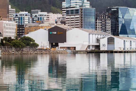 Looking across the waterfront at the TSB arena and Shed 6, 3 large sheds painted white and 1 painted black. The city centre buildings can be seen behind.