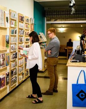 2 people in gallery gift shop looking at magazines on a wooden wall.