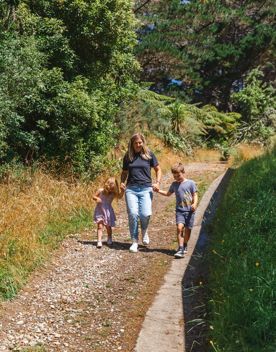 An adult and two kids hold hands while walking along a nature trail.