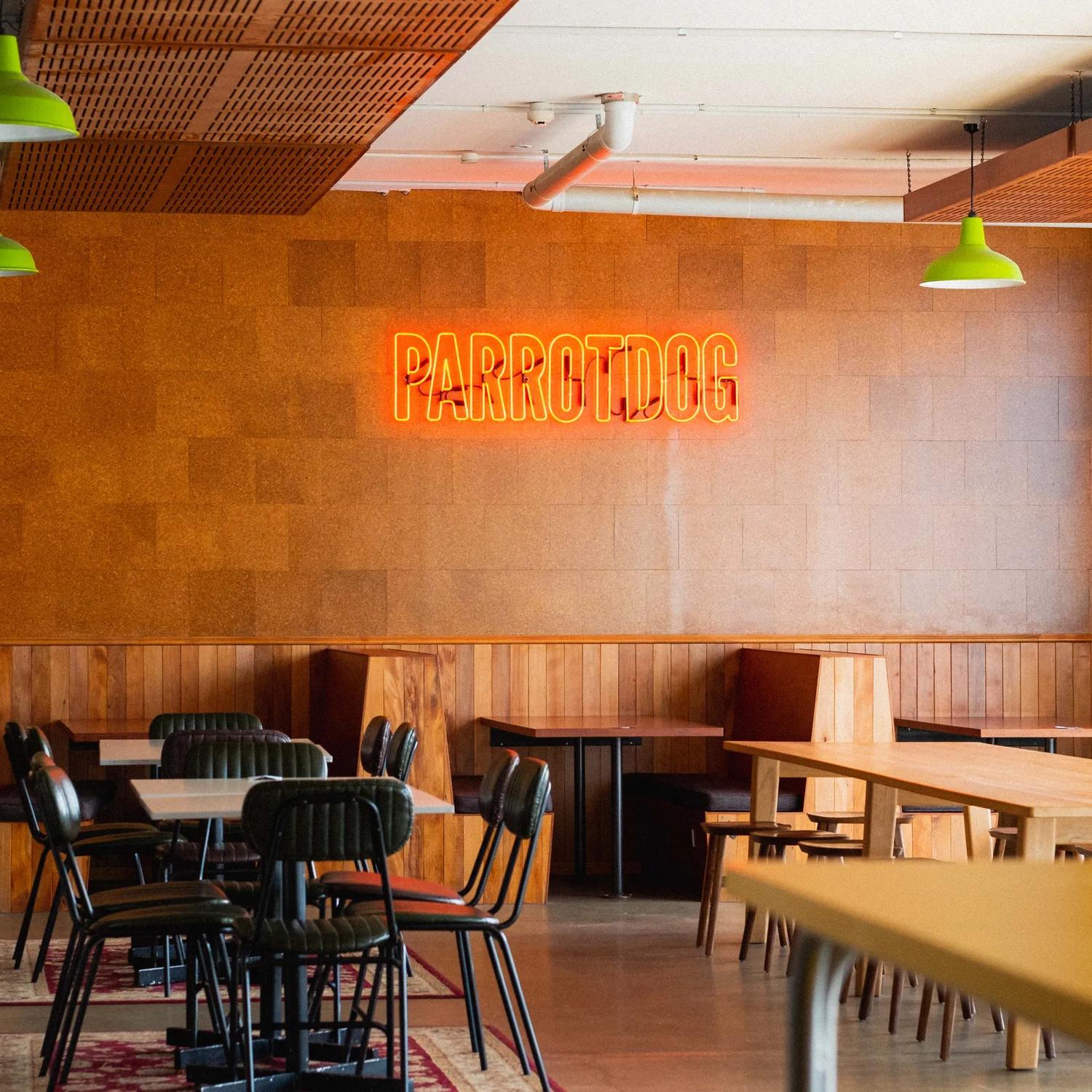 Inside Parrotdog Bar & Brewery there are tables, chairs, wood-panelling, a taxidermied deer head and a neon sign on the wall. 