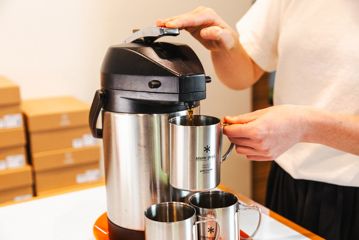 Close up of a person dispensing filter coffee into a stainless steel mug.