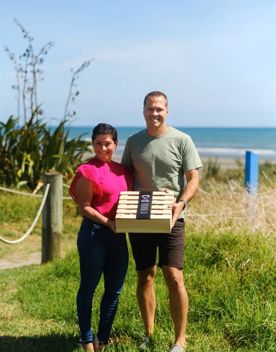 Timo Reitnauer and his wife, Val Reitnauer, stand in a grassy field, holding a wooden box while smiling on a sunny day.