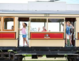 Three children riding on a red and yellow tram in Queen Elizabeth Park, Kāpiti Coast.