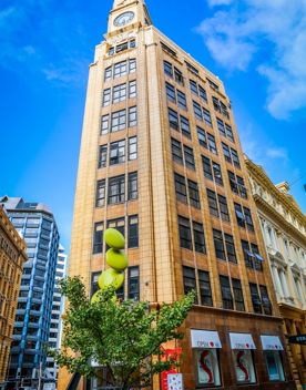 The MLC building at on Lambton Quay in Wellington Central. The yellow-brick building is eight stories tall, with a large clockface at the top.