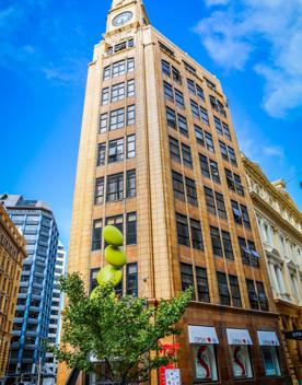 The MLC building at on Lambton Quay in Wellington Central. The yellow-brick building is eight stories tall, with a large clockface at the top. 