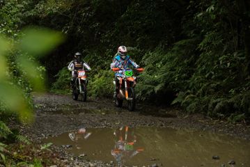Two motor bike riders riding on a trail with puddles.