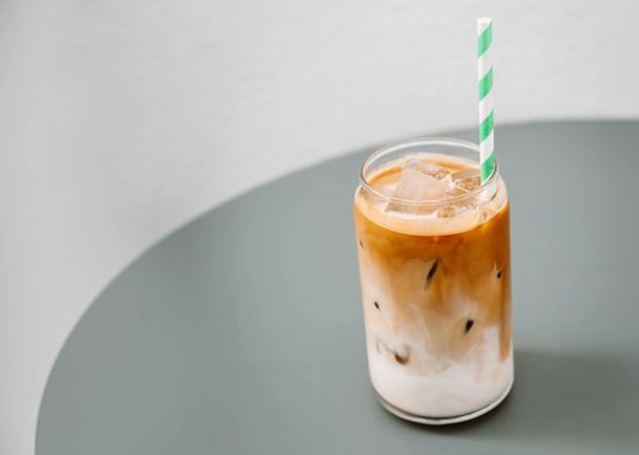 An iced coffee in a glass cup made by West Two espresso, with a green straw.