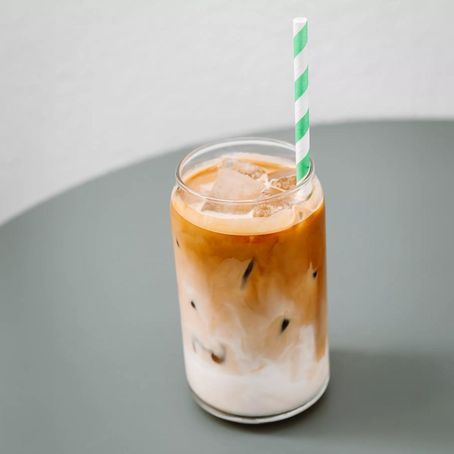 An iced coffee in a glass cup made by West Two espresso, with a green straw.