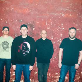 The band members of Mogwai posing against a red wall.