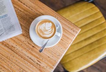 A bird's eye view of a foamy cappuccino in a white coffee cup on a white saucer sitting on a light beige table top at Swimsuit Cafe located on Dixon Street in Wellington.