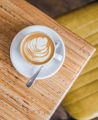 A bird's eye view of a foamy cappuccino in a white coffee cup on a white saucer sitting on a light beige table top at Swimsuit Cafe located on Dixon Street in Wellington.