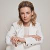 Composer, Gemma New, poses in a white suit in front of a beige backdrop.