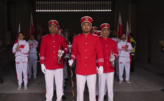 Twelve people in red and white marching band uniforms stand in formation holing flags and horns. 