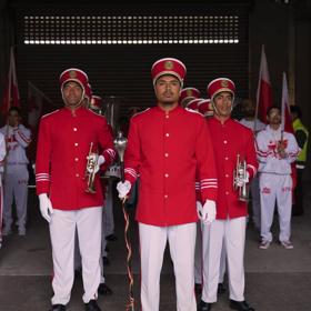 Twelve people in red and white marching band uniforms stand in formation holing flags and horns. 