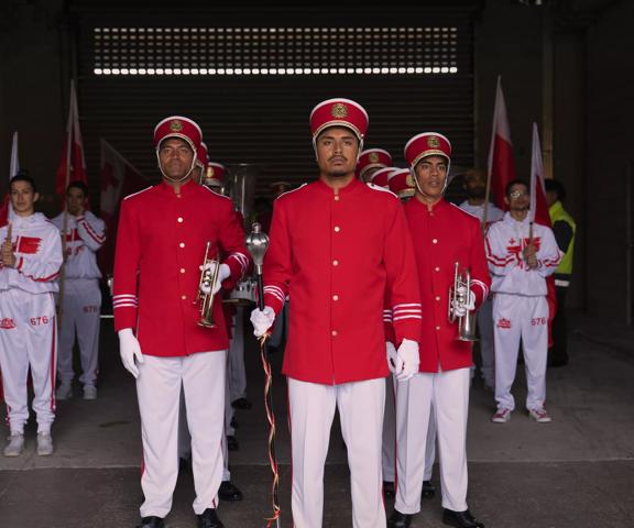Twelve people in red and white marching band uniforms stand in formation holing flags and horns. 