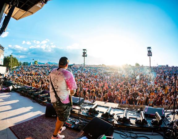 A guitarist on stage playing an outdoor concert to a packed audience.