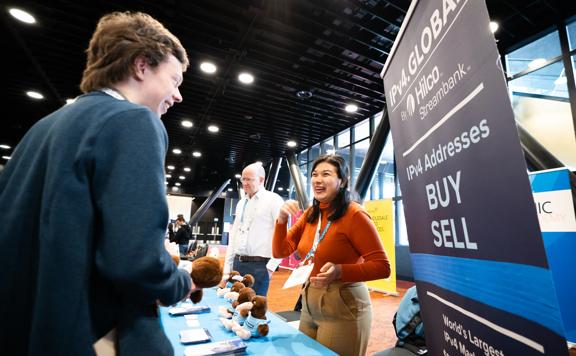 People talk at an information stand at APNIC 58 at Tākina.