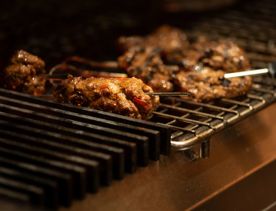 What looks to be meat kebabs grilling on a metal plate at Kisa.