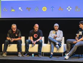 Four speakers on a panel at New Zealand Game Developers Conference sit on couches holding mics.