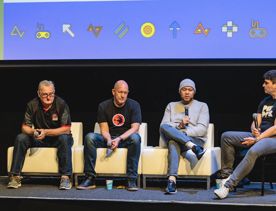 Four speakers on a panel at New Zealand Game Developers Conference sit on couches holding mics.