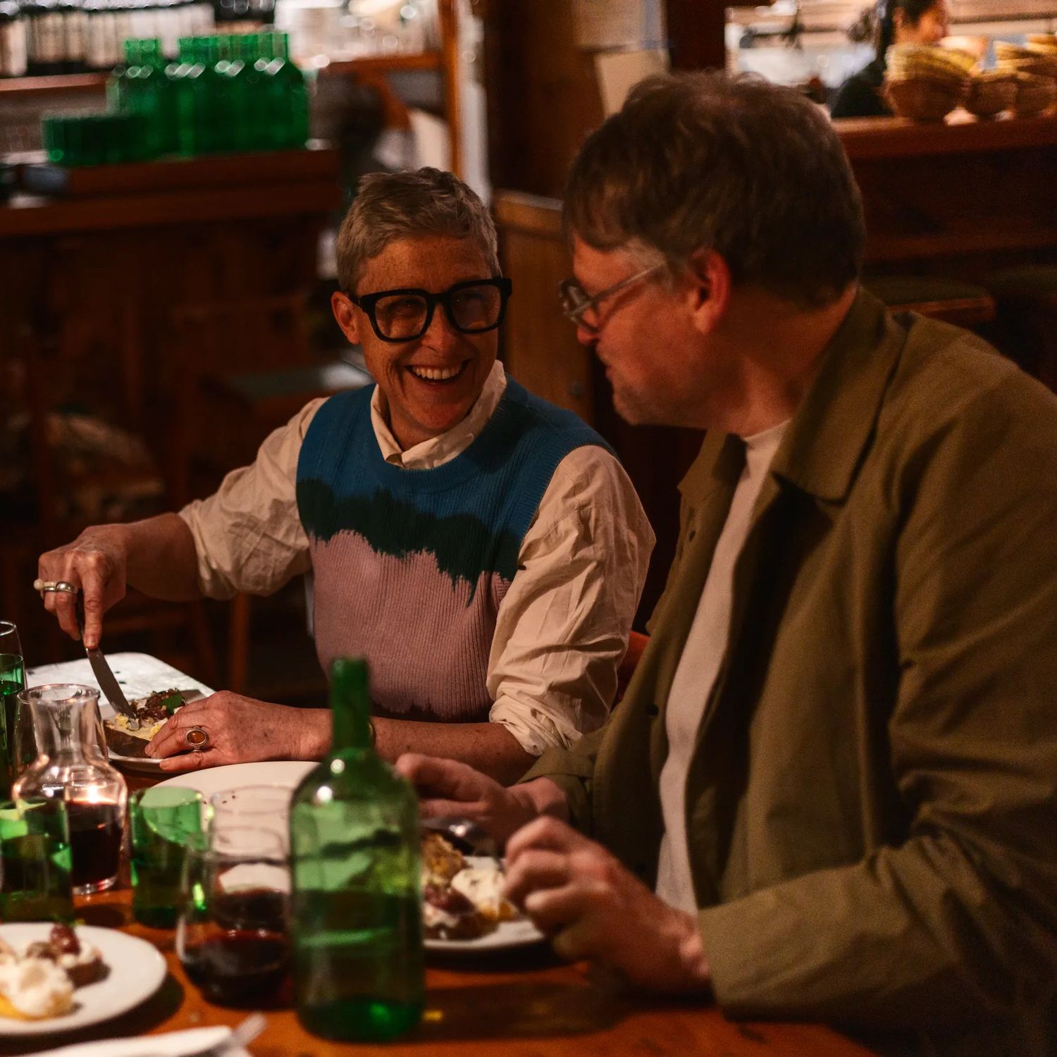 Patrons dining in a warm, intimate restaurant setting with shared plates and drinks.