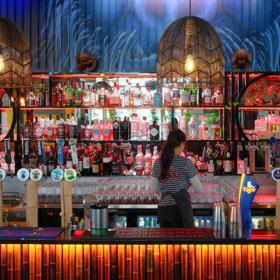 A bartender faces the wall while standing behind a colourful, tiki-style bar.