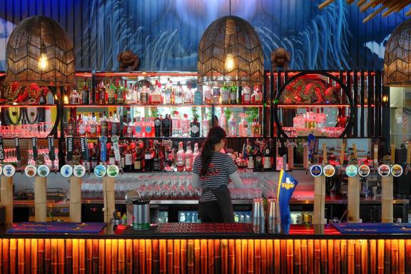 A bartender faces the wall while standing behind a colourful, tiki-style bar.