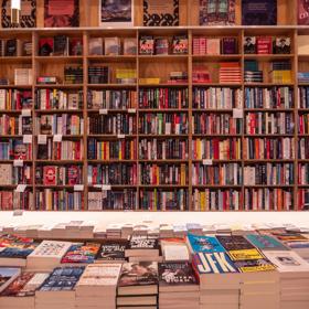 The floor-to-ceiling plywood shelves at Good Books are filled with books. A table in front holds stacks of books.