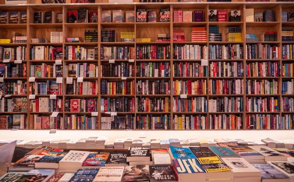 The floor-to-ceiling plywood shelves at Good Books are filled with books. A table in front holds stacks of books.