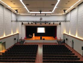 The stage set up for Lower Hutt Events Centre, hundreds of chairs facing forwards, stairs, stage lights, and very high ceilings.