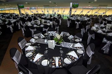 Inside a corporate box at Hnry Stadium Function Centre. Many tables are set with silverware and rugby playbook. The large glass windows at the edge of the room overlook the rugby field.
