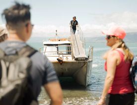 People disembark a boat onto Kapiti Island, with the Kāpiti Coast in the background.