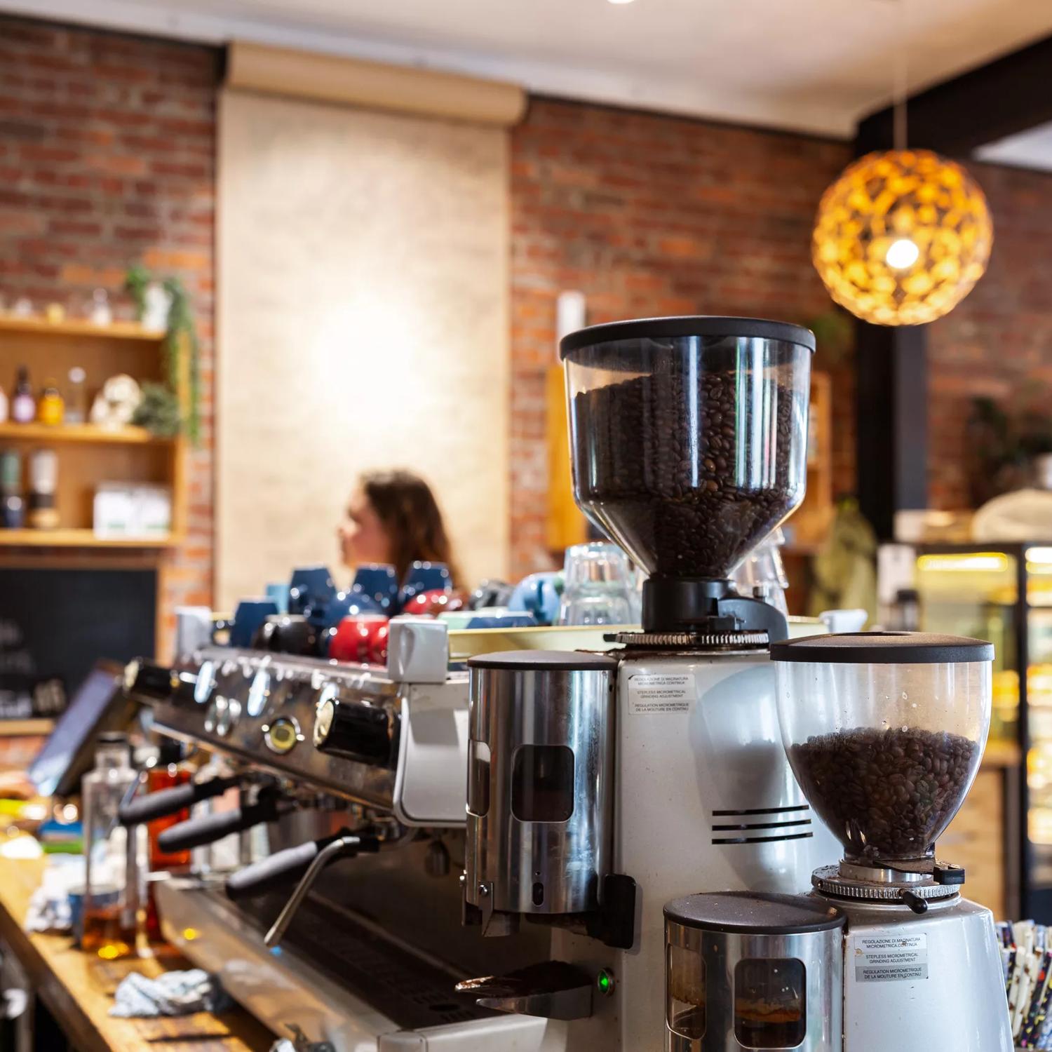 
Inside Caffiend, the counter is L-shaped with a wooden bench. On top sits a coffee machine and a glass cabinet of food. The wall behind is brick with shelving.