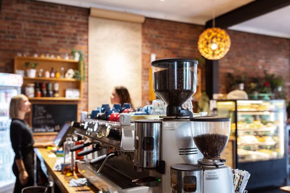 Inside Caffiend, the counter is L-shaped with a wooden bench. On top sits a coffee machine and a glass cabinet of food. The wall behind is brick with shelving.