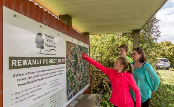 A family reads the information in the hub at Rewanui Forest Park. They are all wearing neon clothing.