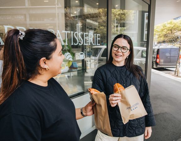 Two people enjoy hot cross buns outside of a bakery.