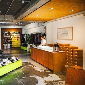 Staff member behind the counter at the Coffee Outdoors Wellington store, with camping and outdoor products on display.