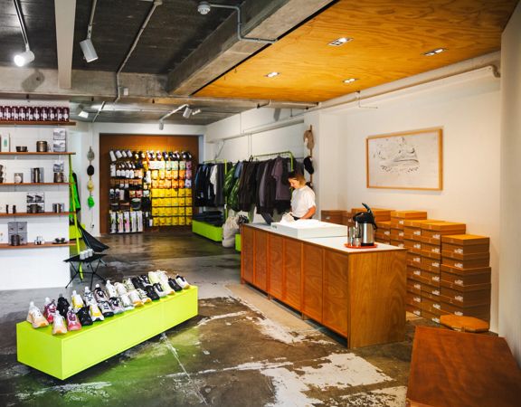 Staff member behind the counter at the Coffee Outdoors Wellington store, with camping and outdoor products on display.