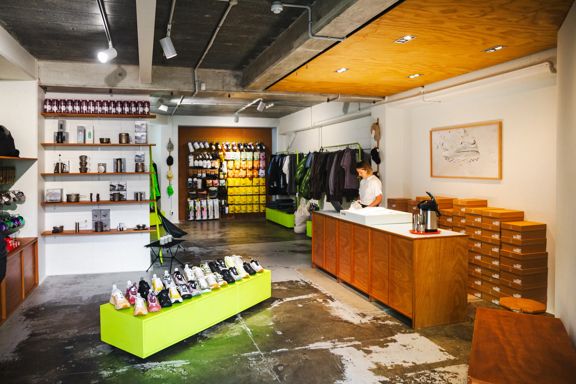 Staff member behind the counter at the Coffee Outdoors Wellington store, with camping and outdoor products on display.