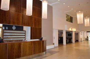 West Plaza Hotel lounge and lobby space with high ceilings, cylindrical chandeliers and a wooden front desk.