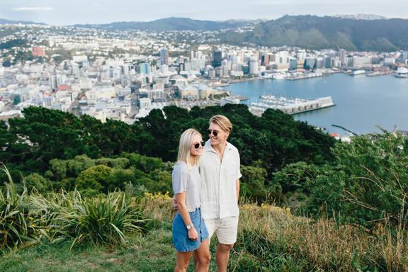 2 people stand close together atop Mount Victoria, and the city of Wellington can be seen behind.