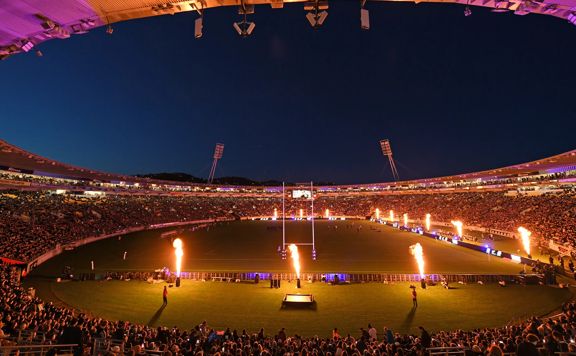 Interior view of the stadium in Wellington showing orange and pink lighting, and large flame displays on the pitch.