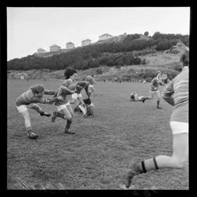 Image form 1959 of women in the midst of a rugby game at Titahi Bay, Wellington. Three separate tackles in motion. Plunket Mothers vs. Kapi-Mana Basketball Club.